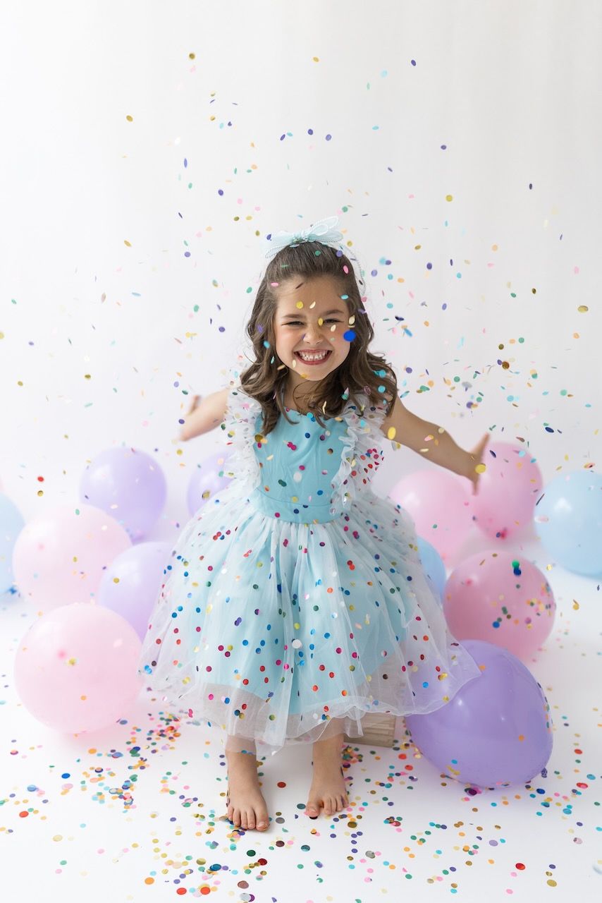 Studio portrait of girl blowing confetti from her hands in a magical birthday moment.