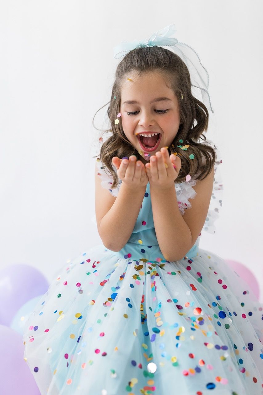 Studio portrait of girl blowing confetti from her hands in a magical birthday moment.