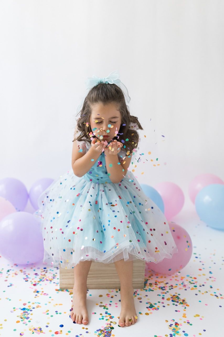 Studio portrait of girl blowing confetti from her hands in a magical birthday moment.