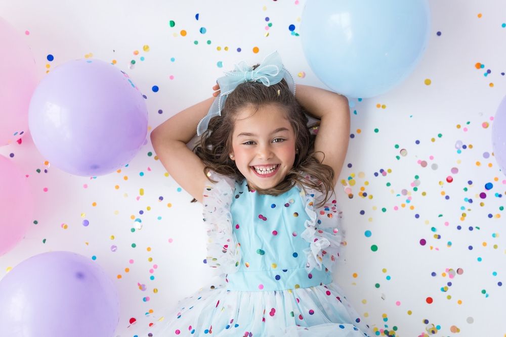 Studio portrait of girl blowing confetti from her hands in a magical birthday moment.
