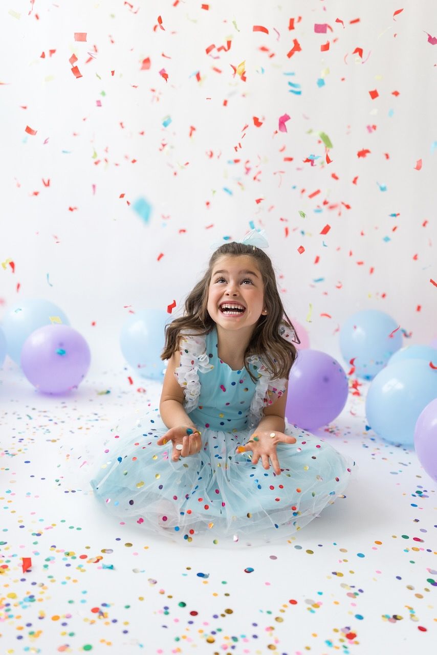 Studio portrait of girl blowing confetti from her hands in a magical birthday moment.