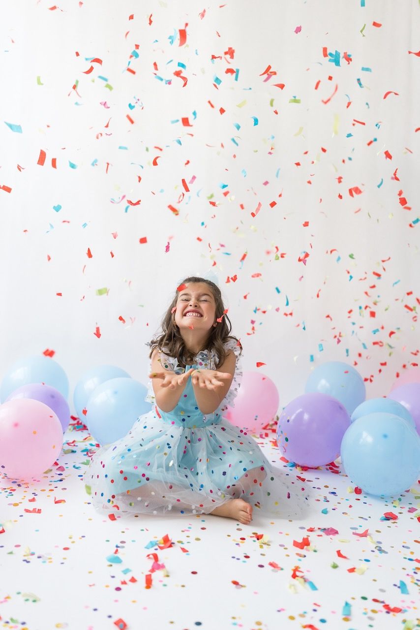Studio portrait of girl blowing confetti from her hands in a magical birthday moment.