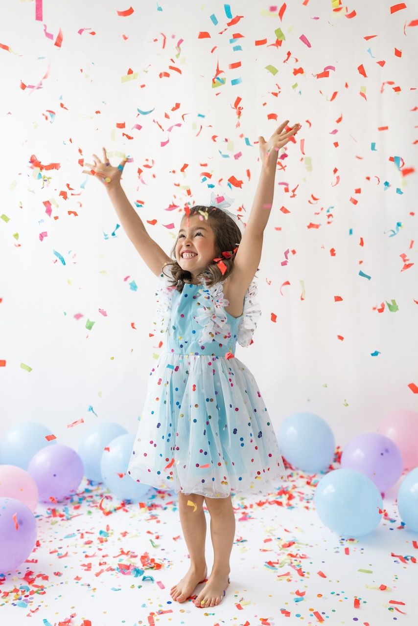 Studio portrait of girl blowing confetti from her hands in a magical birthday moment.