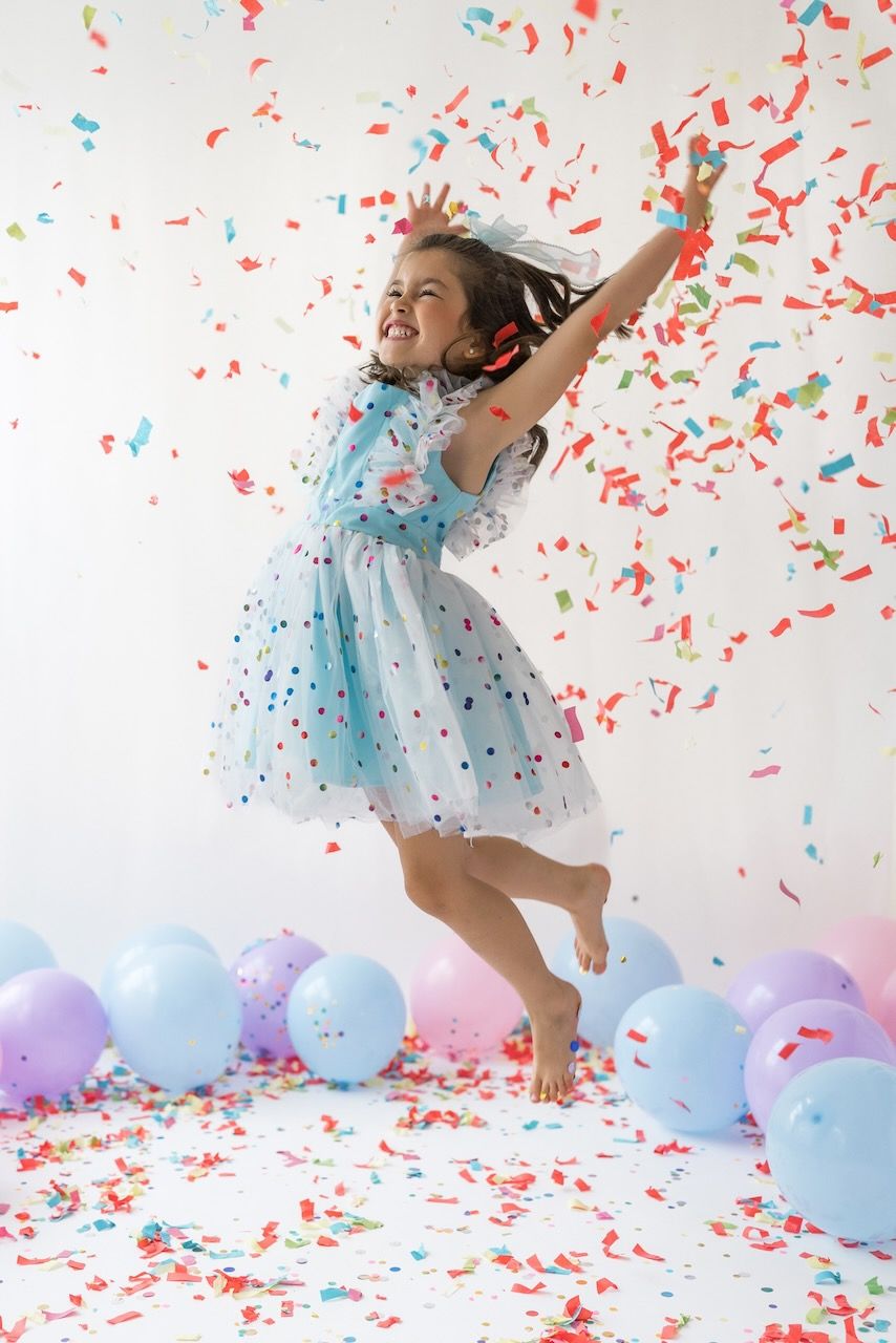 Studio portrait of girl blowing confetti from her hands in a magical birthday moment.