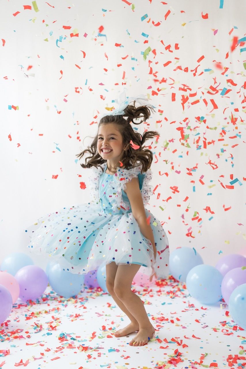 Studio portrait of girl blowing confetti from her hands in a magical birthday moment.