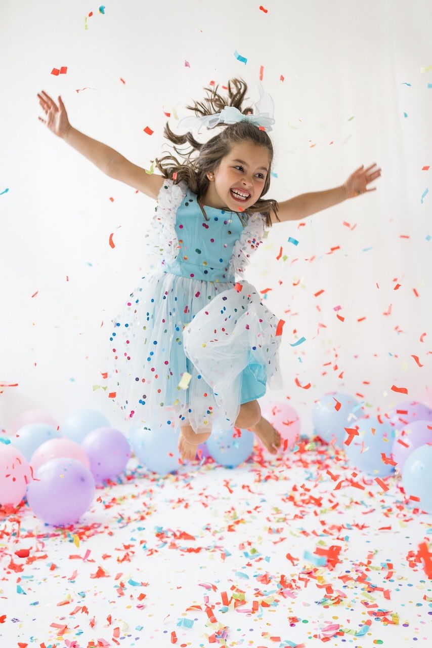 Studio portrait of girl blowing confetti from her hands in a magical birthday moment.