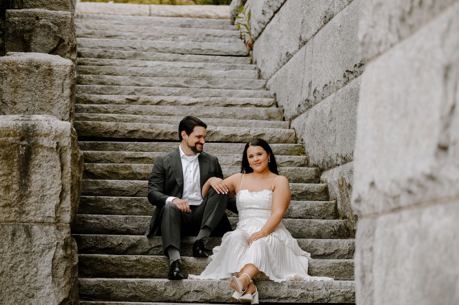 A couple in wedding attire sits together on stone steps during a romantic outdoor photography session.