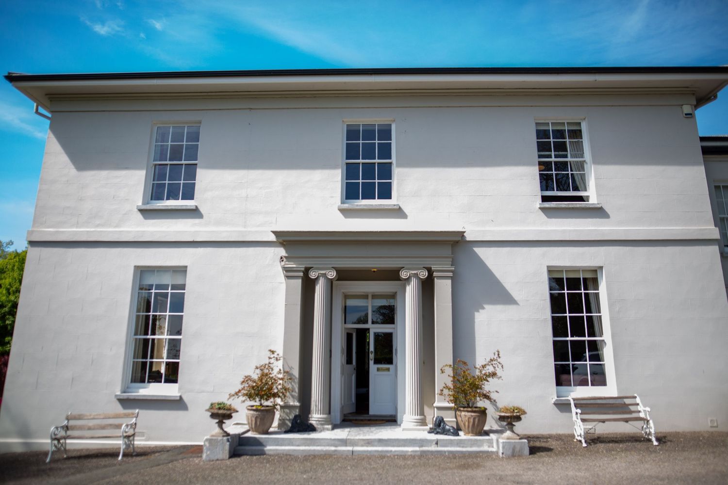 Elegant white coastal house with multiple windows and columns features exterior architectural details against blue sky.