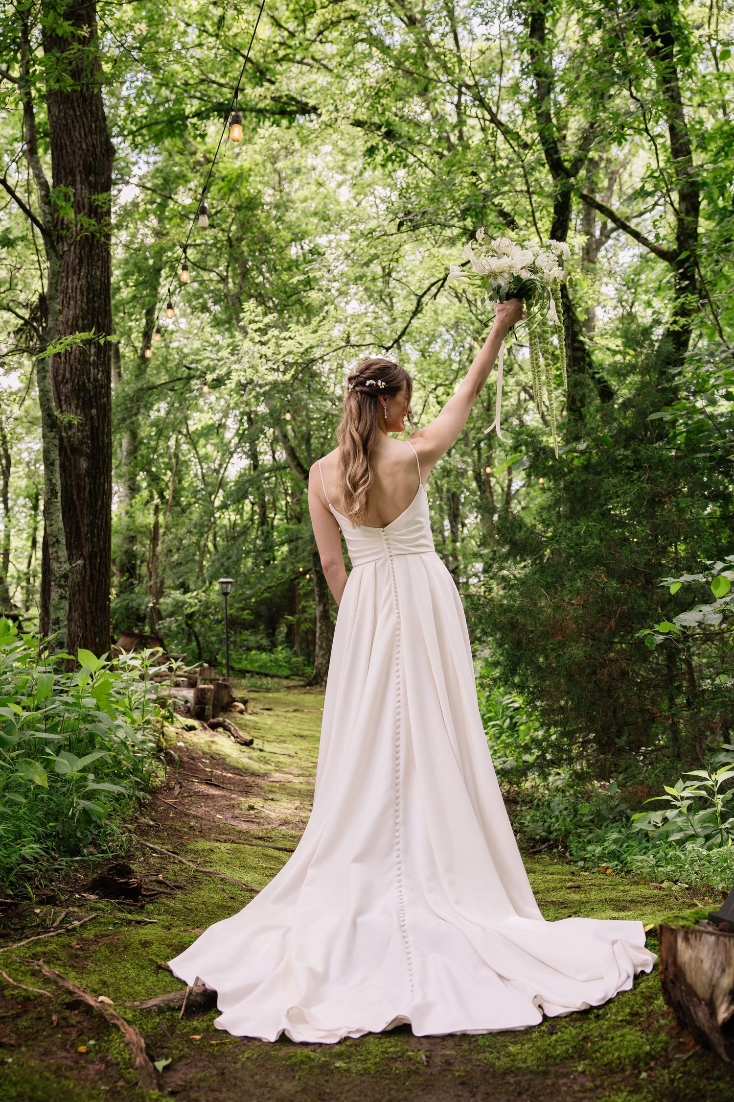 Someone in a flowing white dress dances gracefully through a lush green forest path on a summer day, creating a dreamlike scene.