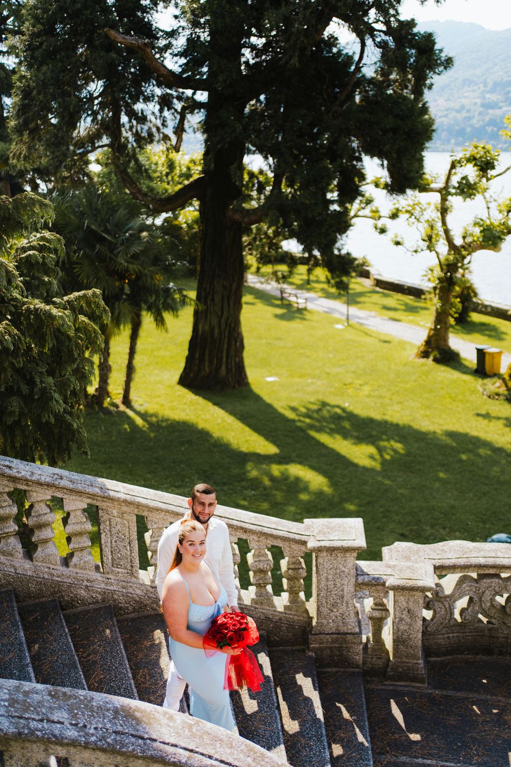 Scenic lakeside stone garden staircase with tall evergreen trees and lush greenery against mountain backdrop.