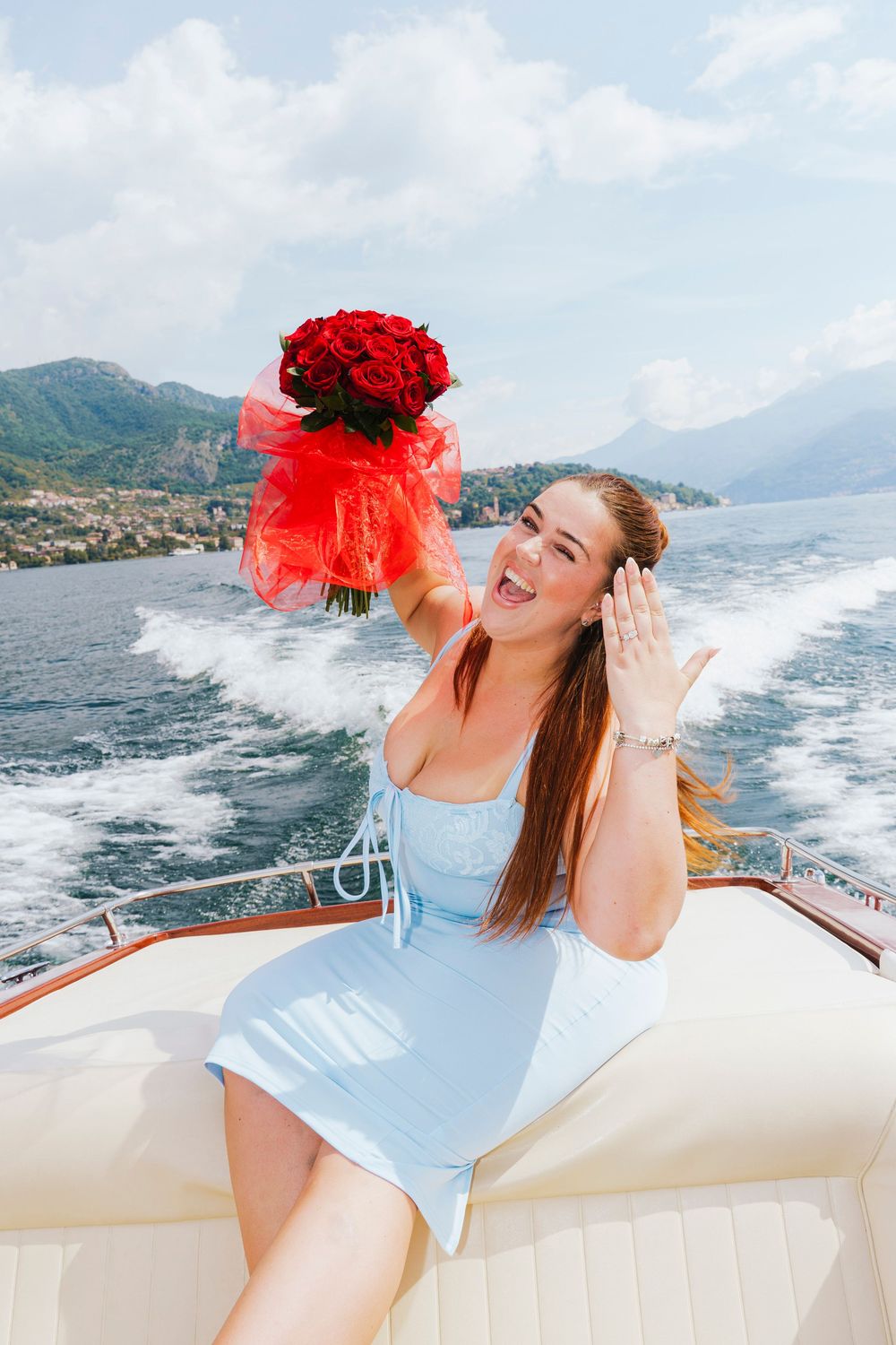 A joyful scene on a boat with a person in a blue outfit holding vibrant red roses against a scenic coastal backdrop.