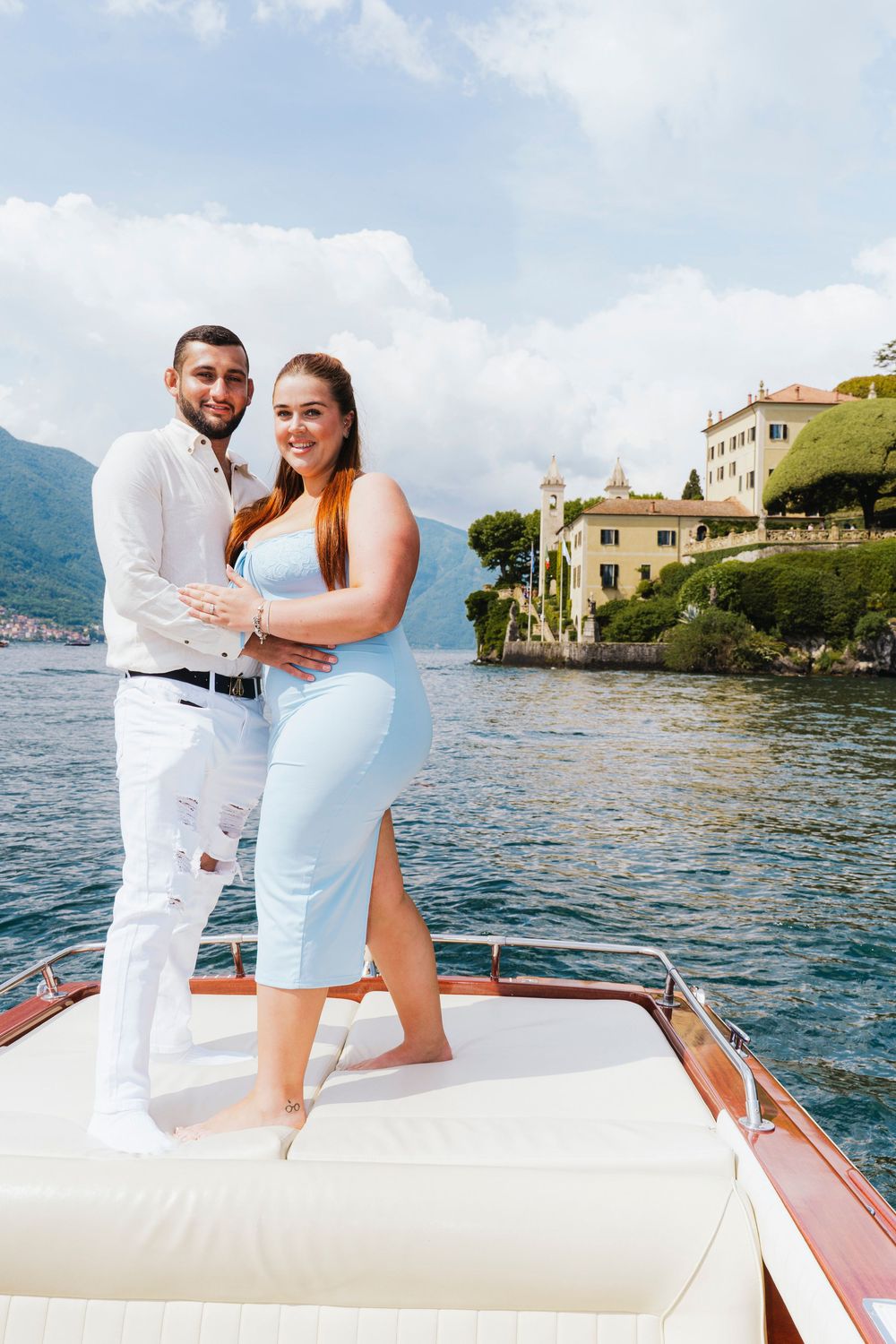 Romantic photoshoot of a couple embracing on a luxurious boat on Lake Como with Villa del Balbianello in the background.