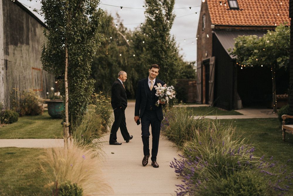 Two people walk along a garden path next to ornamental grasses on a sunny autumn day.