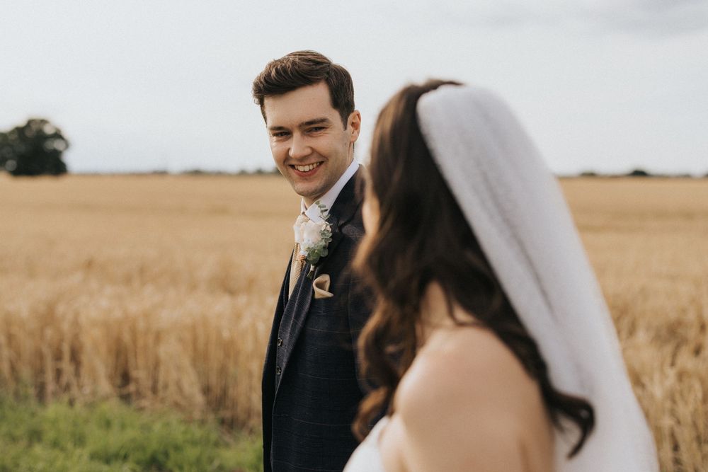 A happy couple in wedding attire share a joyful moment together while standing in a golden wheat field.
