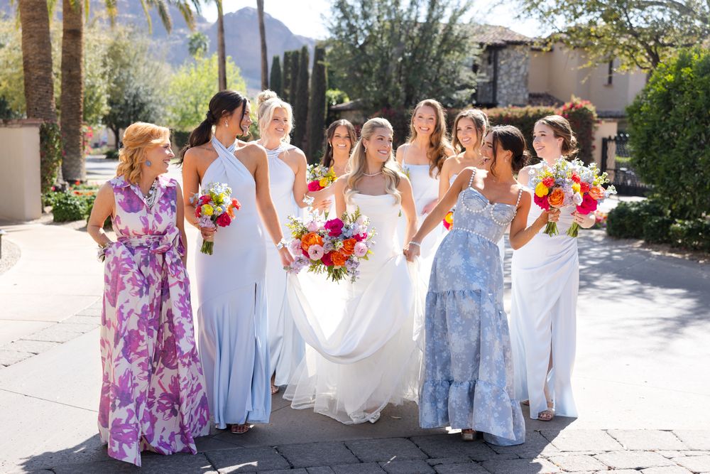 Bridal party in purple and blue dresses posing outdoors with mountains in background.