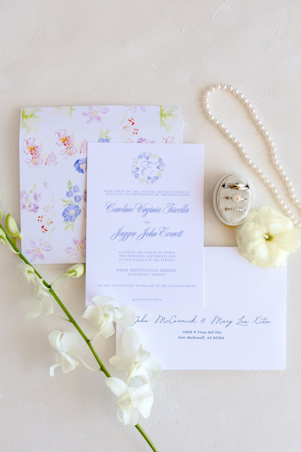 Elegant wedding invitations displayed with delicate white flowers and pearl necklace on a light background.