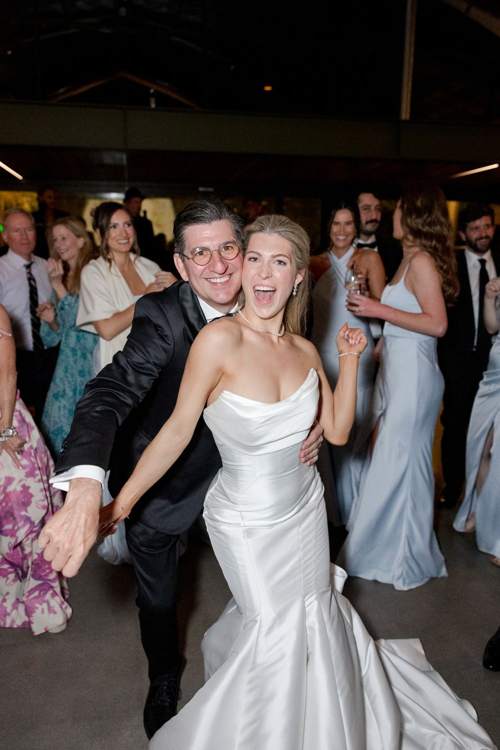 Happy wedding guests dancing and celebrating together at a reception with bridesmaids in blue dresses.