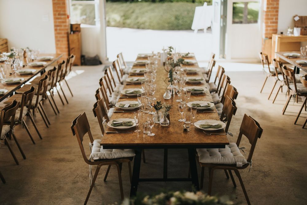 Place settings and wooden chairs line rustic tables inside an elegant farm-to-table restaurant interior.
