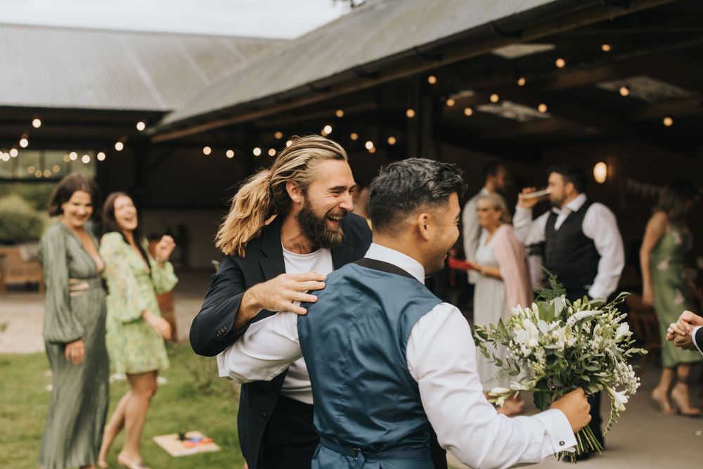 Wedding guests mingle and celebrate during an outdoor reception with twinkling lights and greenery.