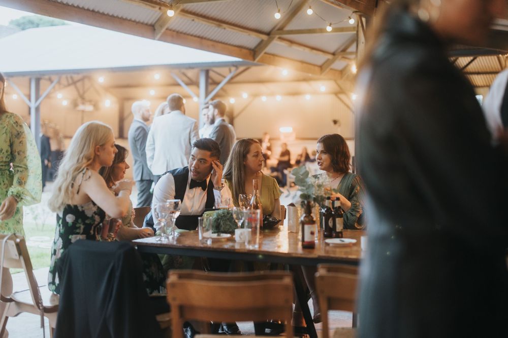 Wedding guests mingle and socialize at an elegant indoor reception venue with warm lighting and white decor.