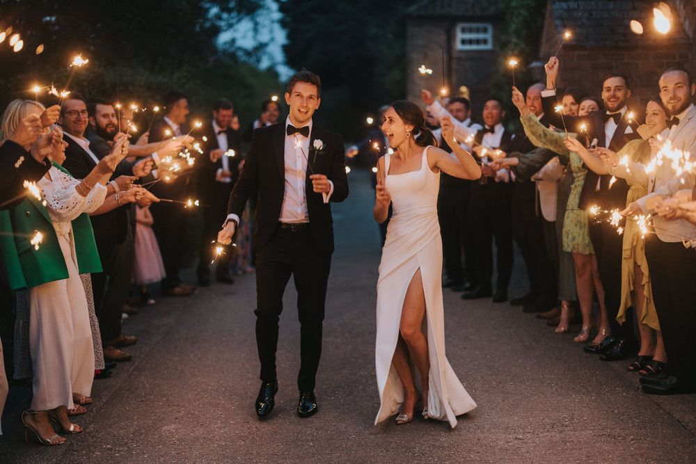 A newlywed couple walks through a sparkler sendoff line at their evening wedding celebration.