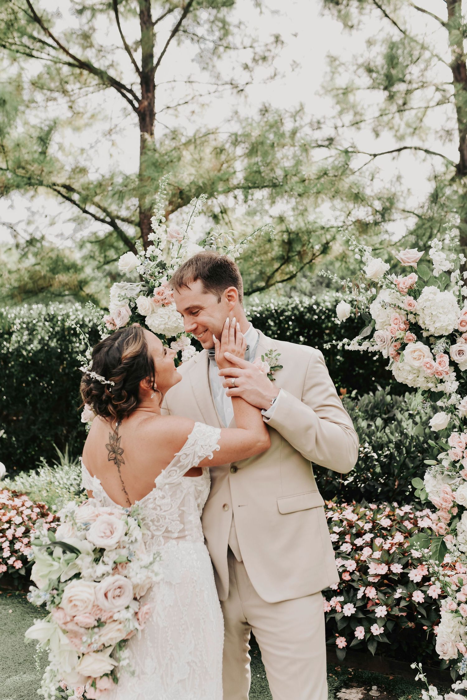 a bride romantically touches her grooms face as they laugh and smile at each other posing for wedding photos