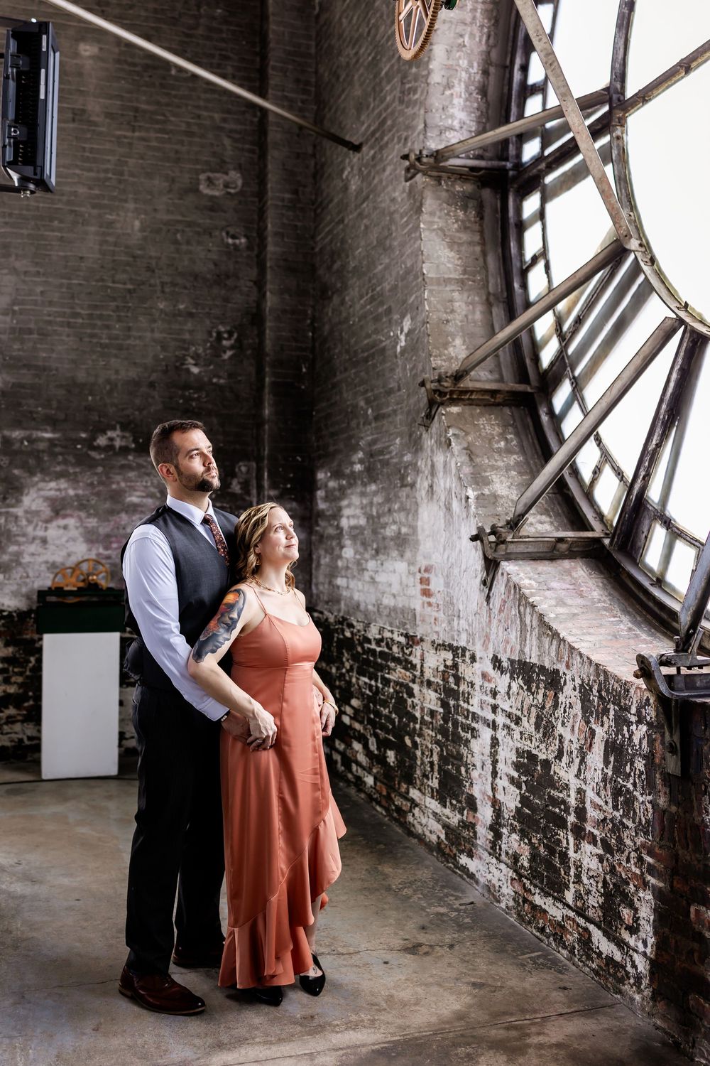 A tender moment shared between two figures in an industrial brick space with angled windows casting dramatic light.