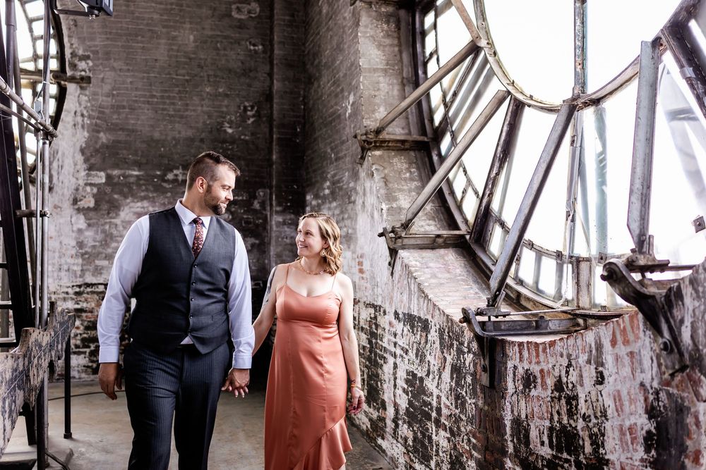 Couple shares romantic moment in rustic industrial venue with exposed brick walls and vintage machinery.