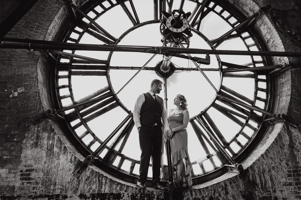 Silhouetted figures stand in front of large illuminated clock face in historic tower.