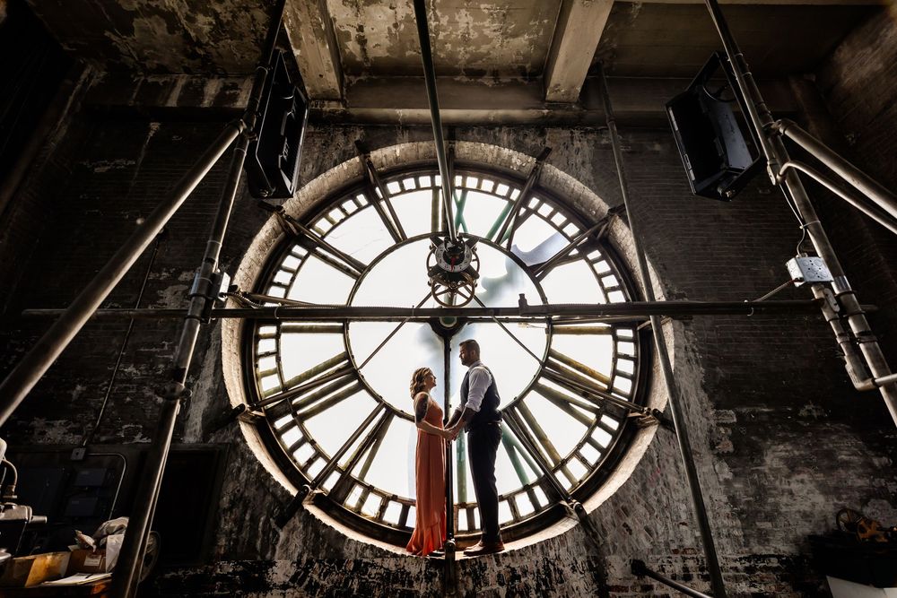 Historic clock tower interior shows illuminated timepiece with dramatic silhouette against backlight.