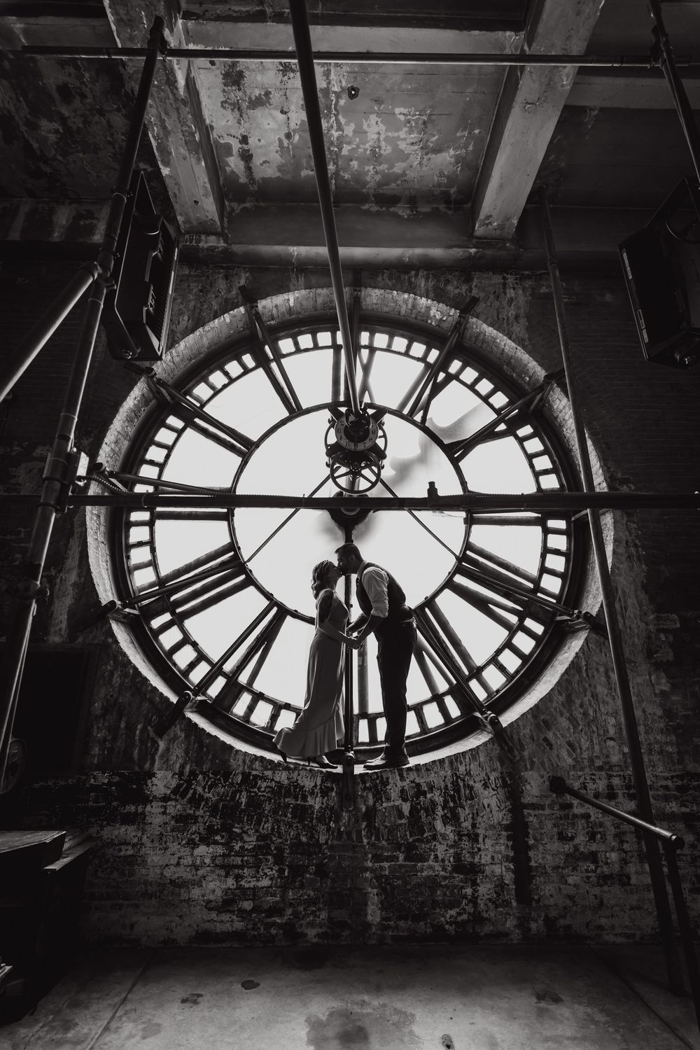 Black and white architectural photograph showing illuminated clock faces against a dark brick wall background.