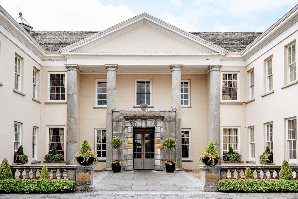 Elegant white manor house with grand pillared entrance, symmetrical windows, and manicured topiary gardens.