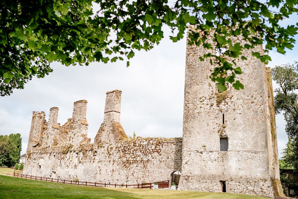 Ancient stone castle ruins surrounded by lush green trees and gardens at sunset create a romantic landscape.