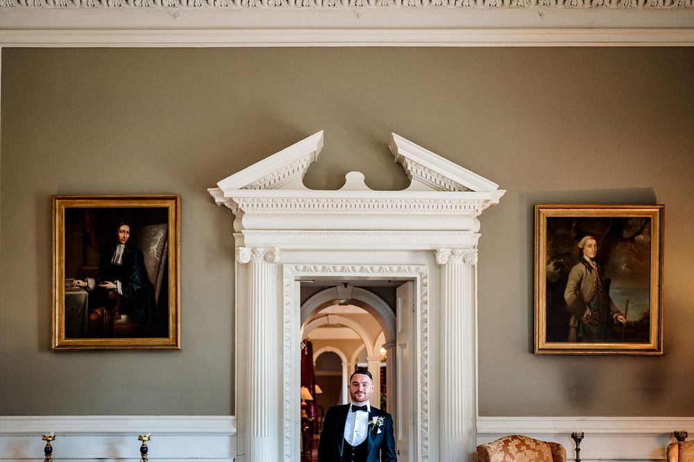 Elegant white doorway with ornate architectural details flanked by two classical portraits in gilded frames in a formal room.
