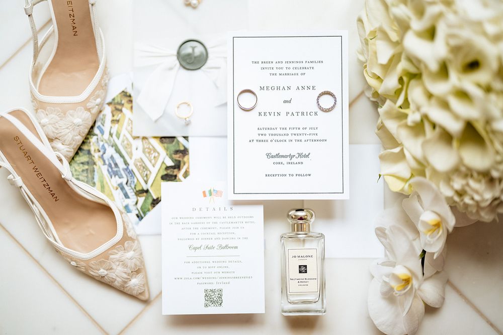 Elegant wedding flatlay with white hydrangeas, invitation cards, perfume bottle and bridal shoes against cream background.