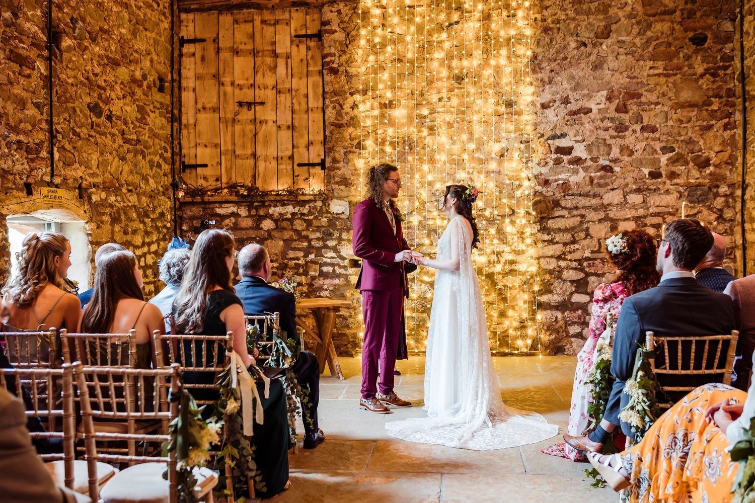 Wedding guests gather in a rustic brick venue during a ceremony with natural lighting streaming through windows.