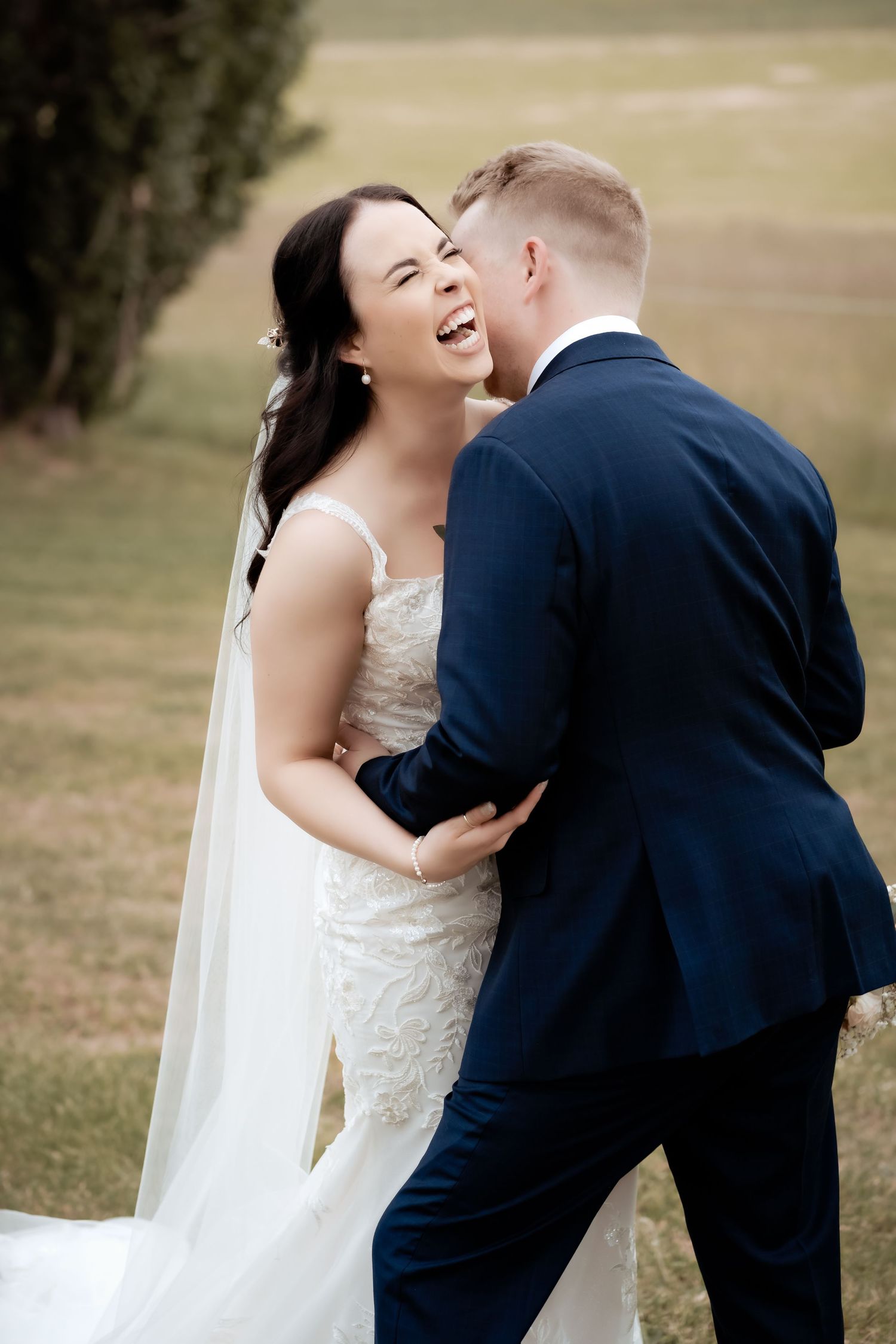 Candid wedding moment captured with natural laughter in an outdoor setting.