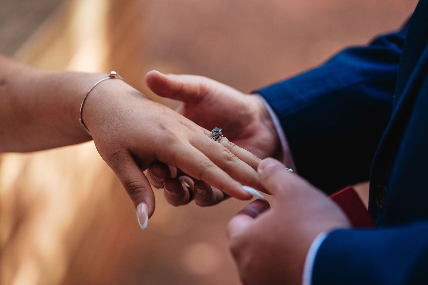 A close-up of hands exchanging wedding rings during a ceremony, with a diamond engagement ring visible.
