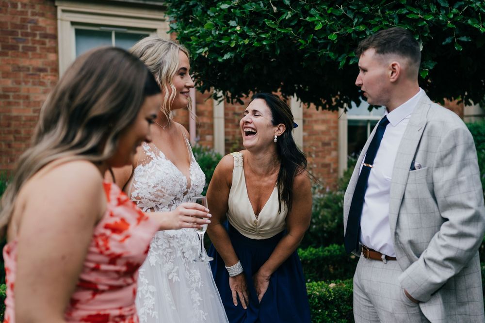 Wedding guests joyfully celebrate and interact during an outdoor reception in front of a brick building.