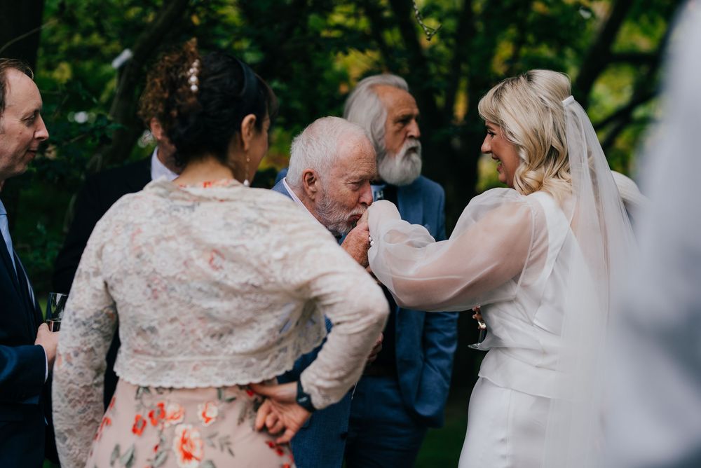 Emotional moment at an outdoor wedding ceremony as people embrace and share heartfelt reactions in a garden setting.