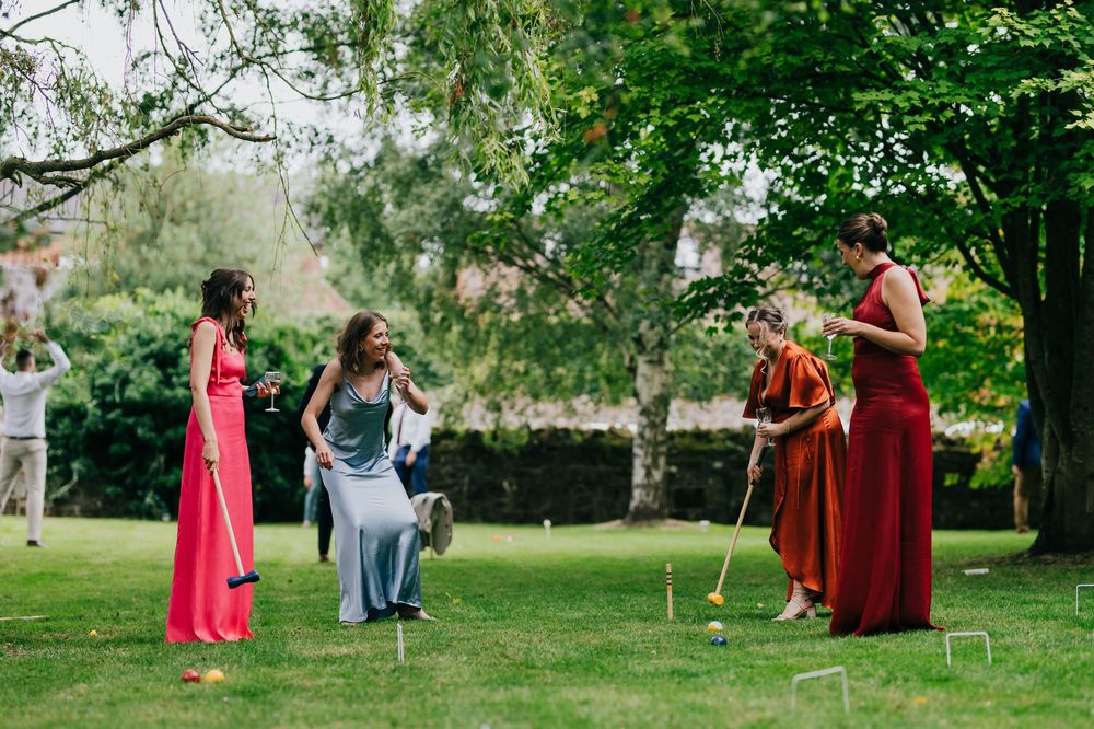 People in red and blue attire playing croquet on a lush green lawn during a sunny summer day.