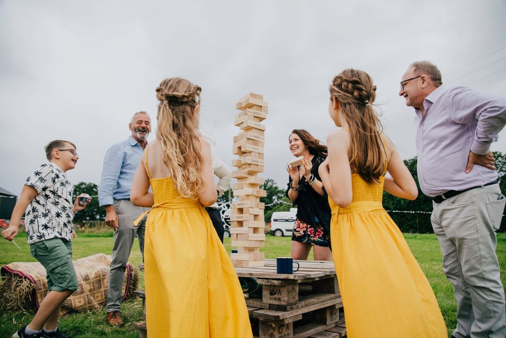 A group of people in bright yellow dresses play a giant Jenga game outdoors on a cloudy day.