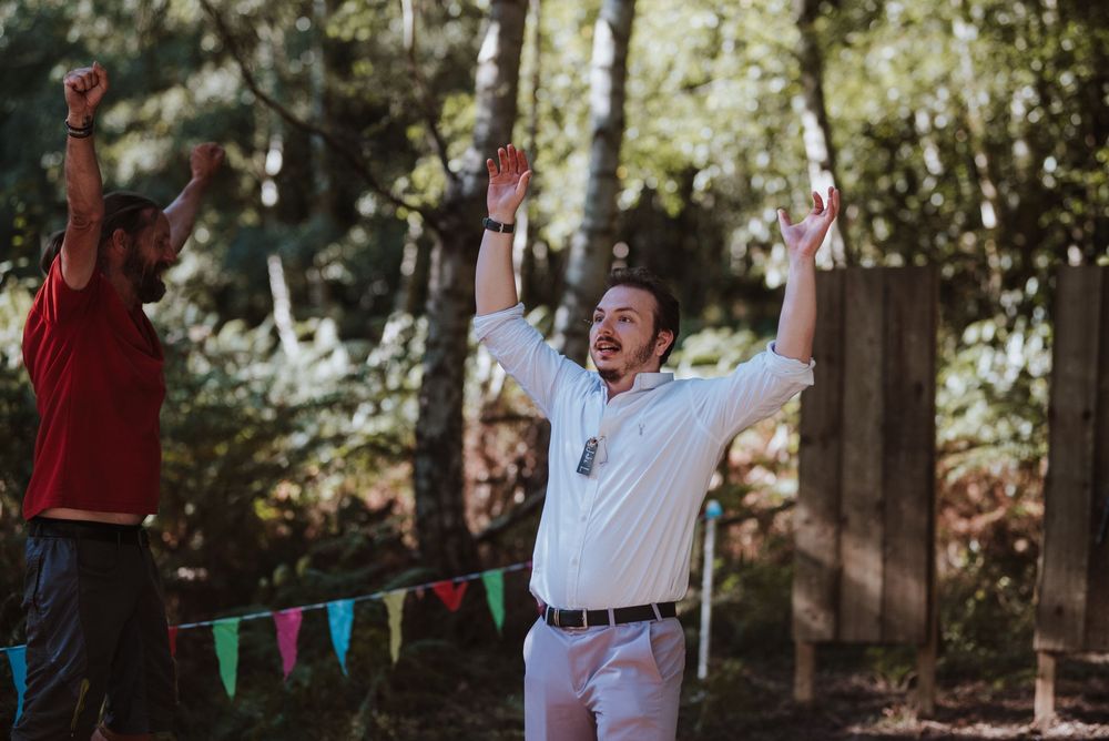 People celebrate outdoors under trees with colorful bunting flags and party decorations at a forest gathering.