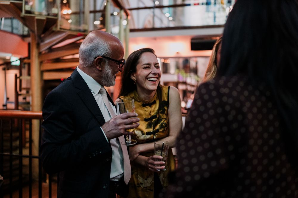 People mingling and conversing at a dimly lit social gathering with warm ambient lighting and festive atmosphere.