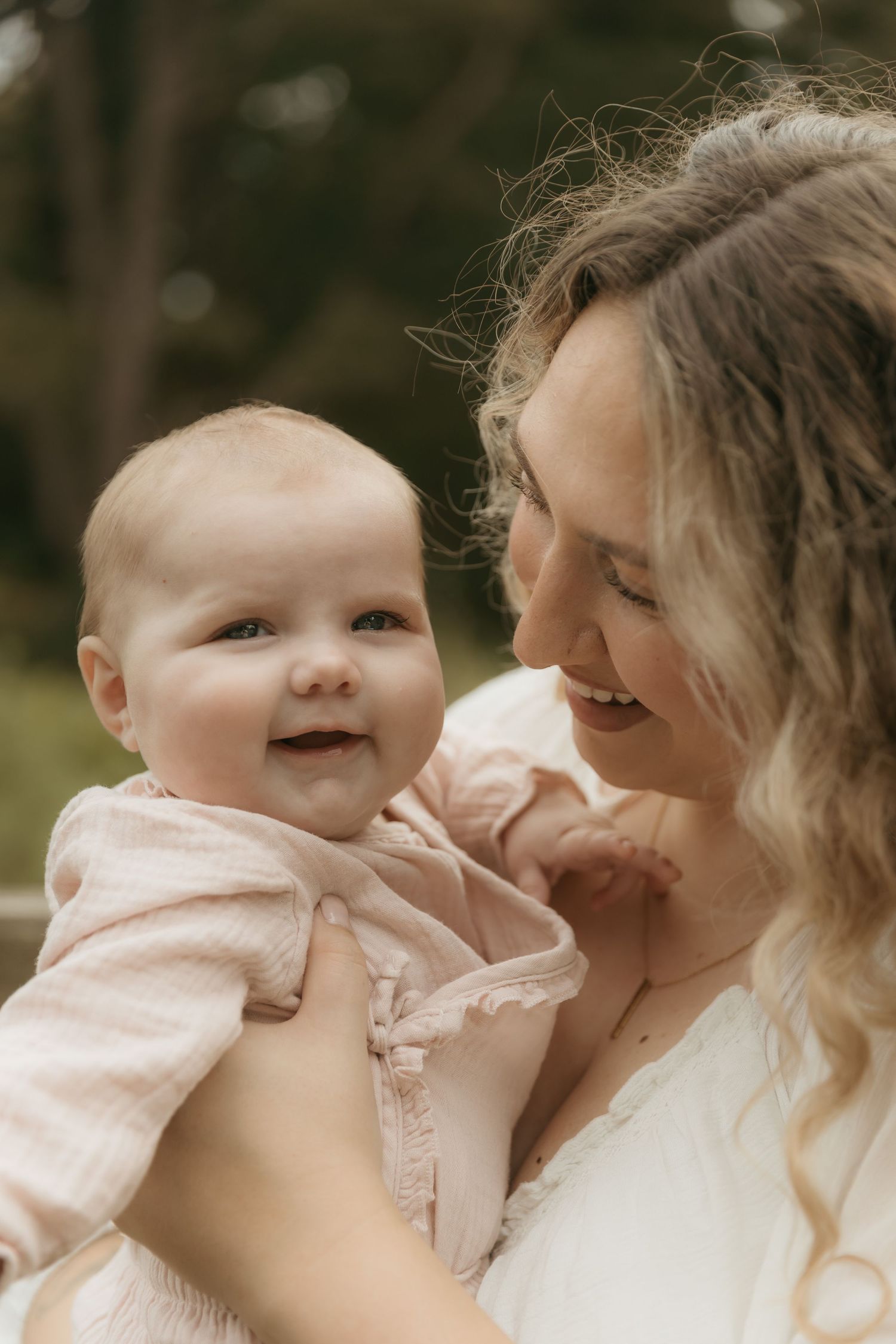 A joyful moment captured in a field of tall grass as a mother wearing white embraces her baby in sweet affection.