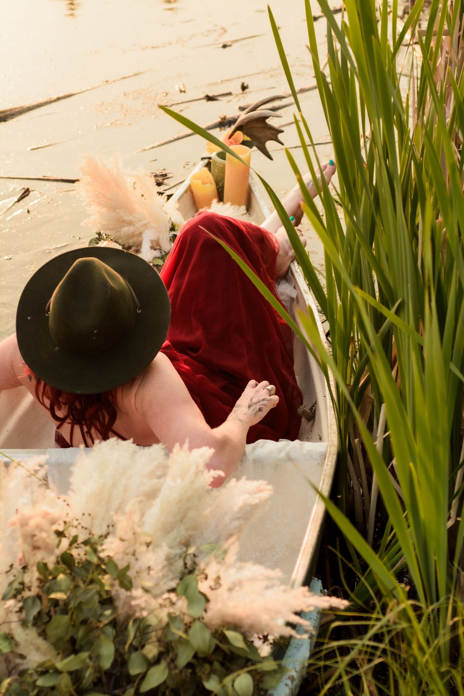 Person in black hat and red dress sitting among ornamental grasses and pampas plumes in garden setting.
