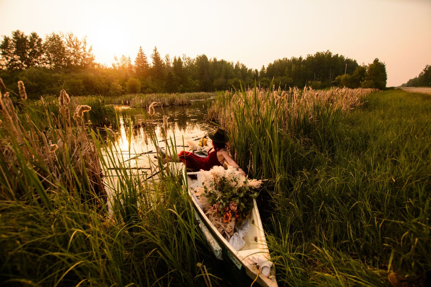 Wedding couple embraces on a dock at sunset surrounded by tall reeds and golden light.