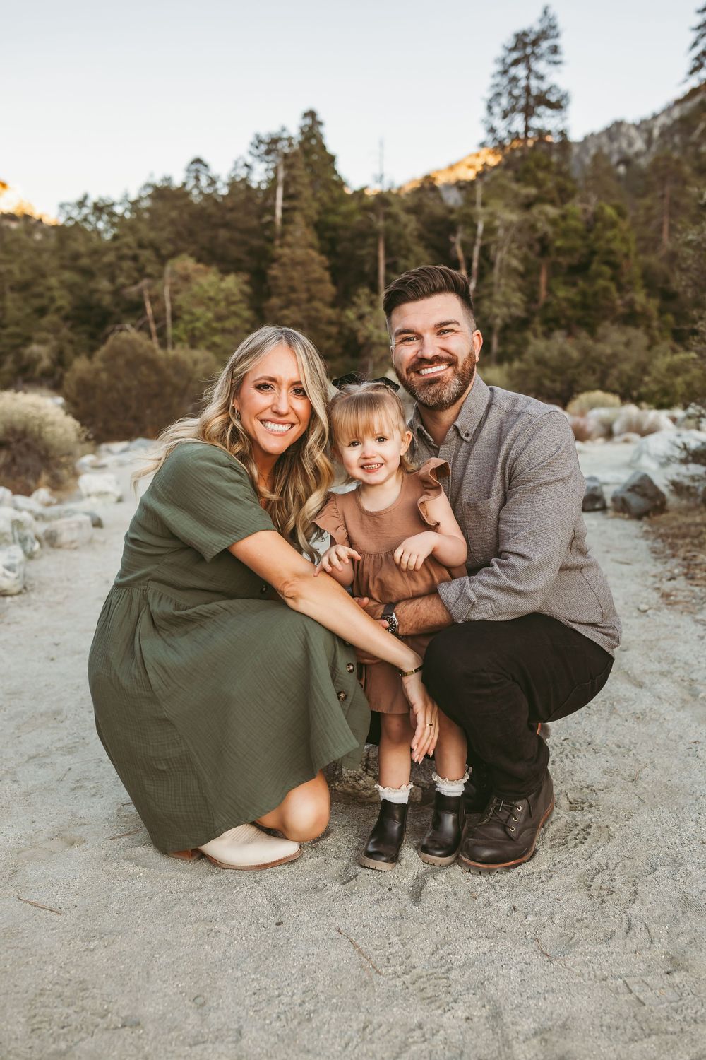 A family poses together against a scenic mountain backdrop with pine trees during golden hour.