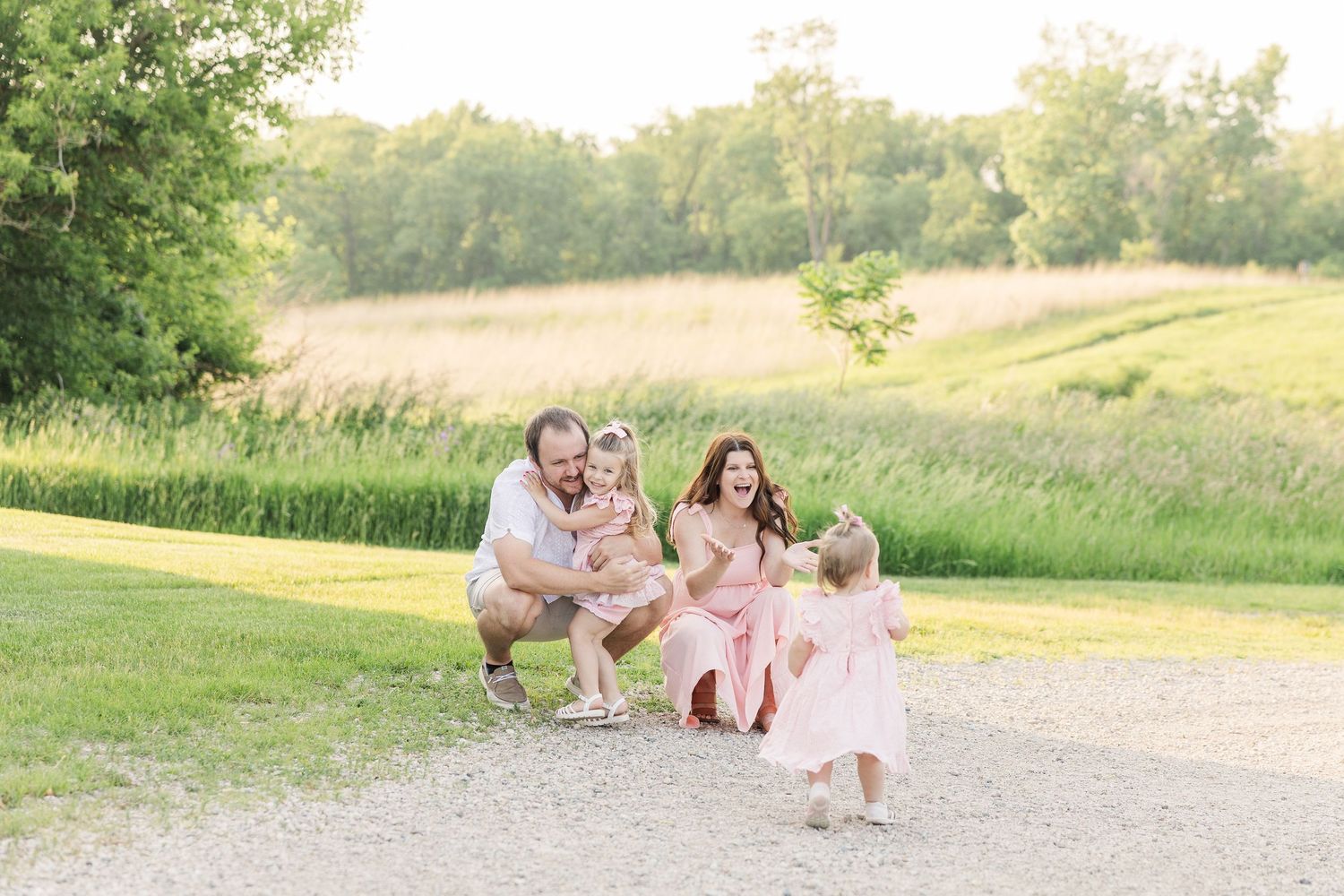 A family stands together on a gravel path in front of a rustic barn with wooden siding and small windows.