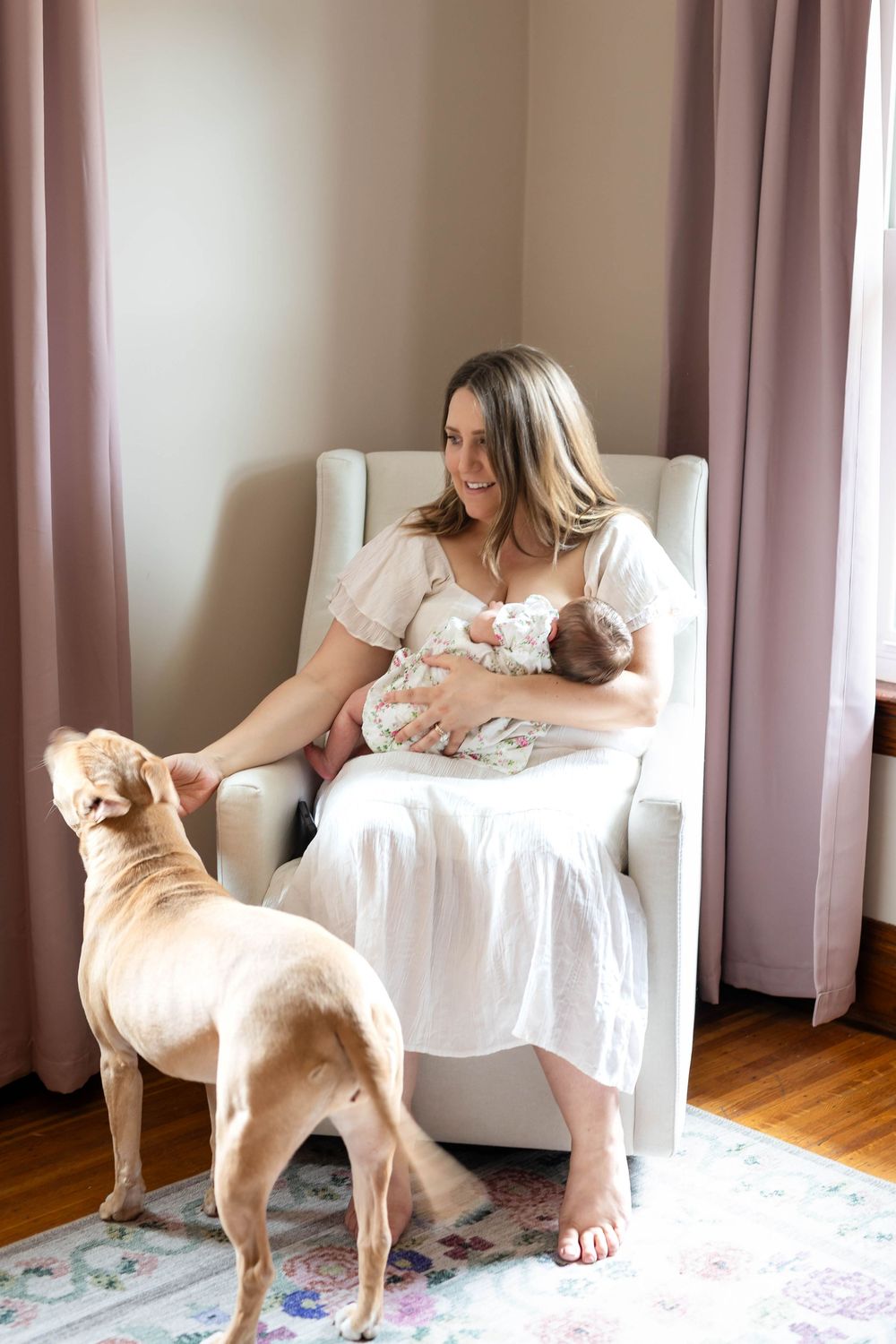 Peaceful nursery scene with a person in white dress sitting in rocking chair with baby and dog.